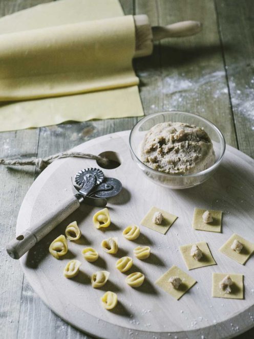 Tortellini alla bolognese in preparazione: sfoglia fresca, ripieno e tortellini già formati su asse infarinato