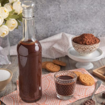 Liquore al cioccolato in bottiglia di vetro servito in un bicchierino, con cacao in polvere e biscotti