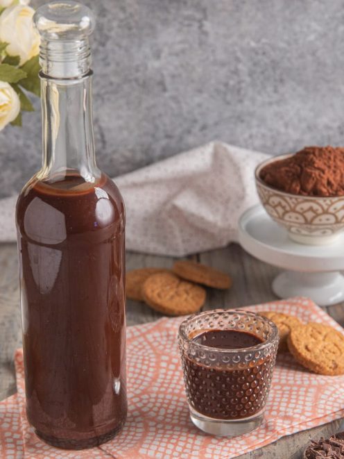 Liquore al cioccolato in bottiglia di vetro servito in un bicchierino, con cacao in polvere e biscotti