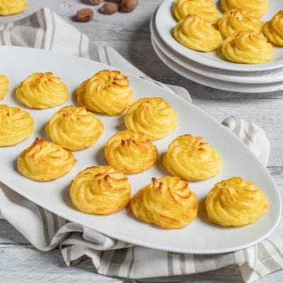Patate duchessa dorate al forno, spuntonate a spirale e servite su vassoio da portata