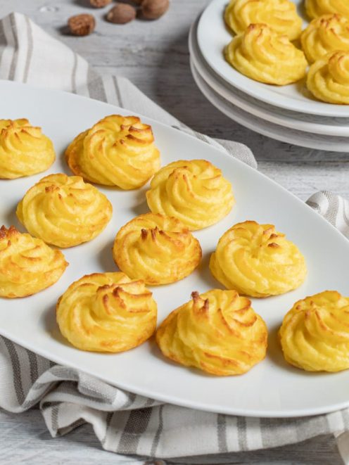 Patate duchessa dorate al forno, spuntonate a spirale e servite su vassoio da portata
