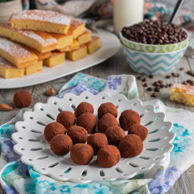 Truffles al caffè ricoperti di cacao amaro, serviti con mandorle e fette di pan di Spagna sullo sfondo