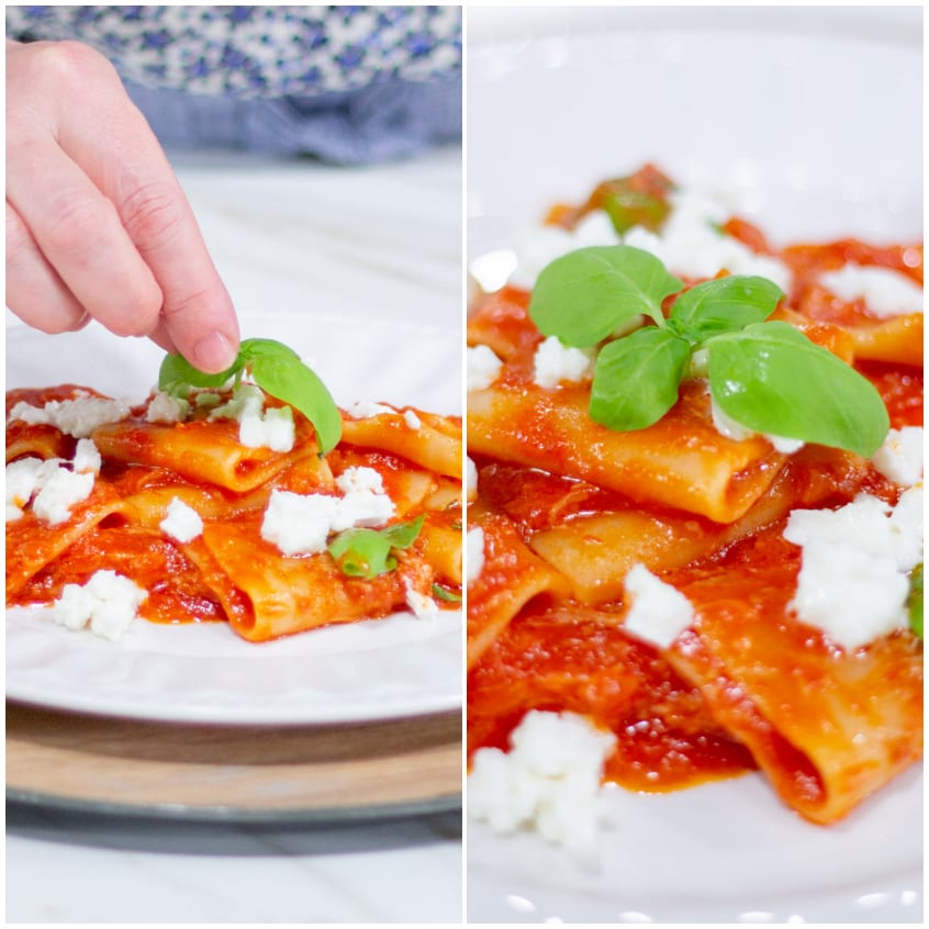 Una mano aggiunge foglie di basilico sui paccheri al pomodoro con ricotta sbriciolata