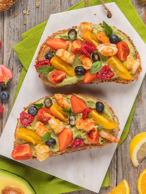 Avocado toast con gamberi, frutti di bosco e pomodorini su pane integrale ai cereali