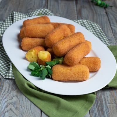 Crocchette di patate fritte dorate servite con una spezzata che mostra il ripieno morbido e foglioline fresche