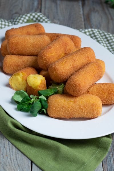 Crocchette di patate fritte dorate servite con una spezzata che mostra il ripieno morbido e foglioline fresche