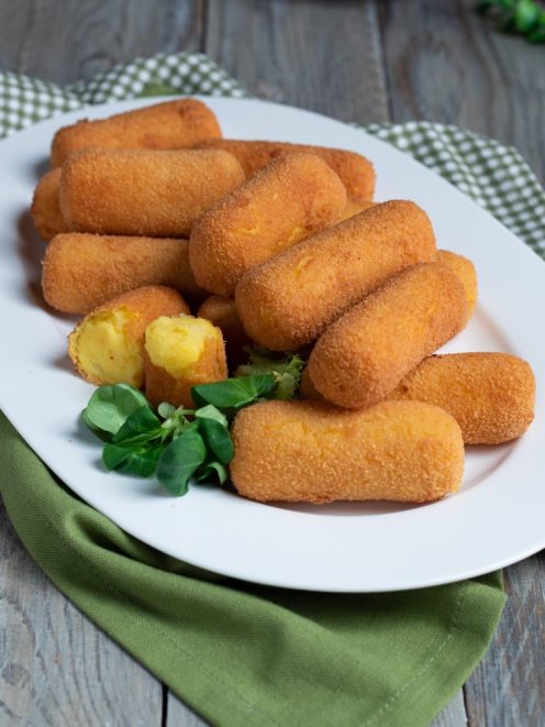 Crocchette di patate fritte dorate servite con una spezzata che mostra il ripieno morbido e foglioline fresche