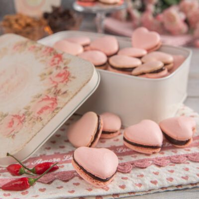 Macaron al cioccolato e peperoncino a forma di cuore con ganache scura, affiancati da peperoncini rossi freschi