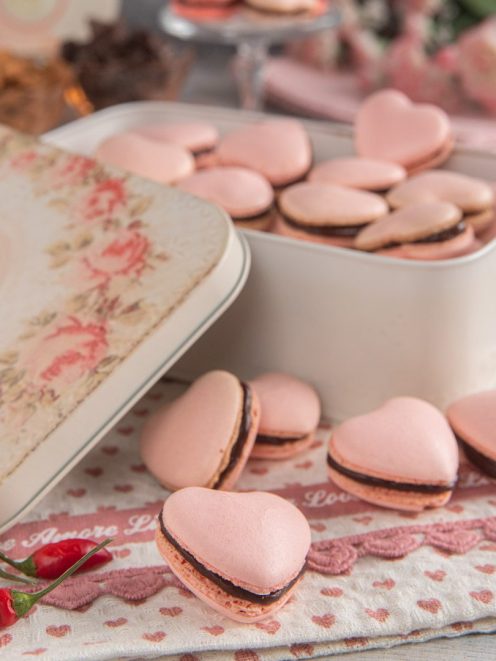 Macaron al cioccolato e peperoncino a forma di cuore con ganache scura, affiancati da peperoncini rossi freschi