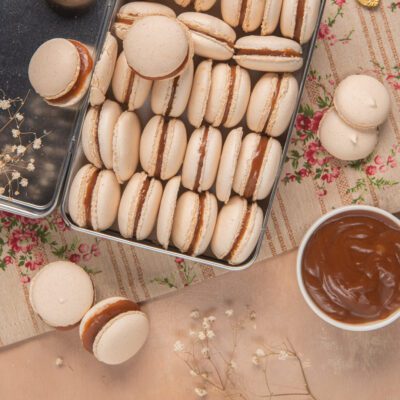 Macarons al caramello salato disposti in fila con il ripieno ben visibile e una ciotola di caramello a lato