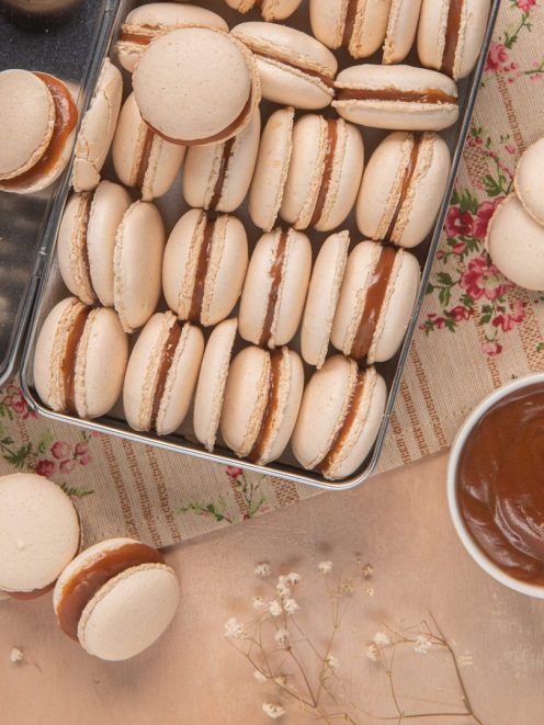 Macarons al caramello salato disposti in fila con il ripieno ben visibile e una ciotola di caramello a lato