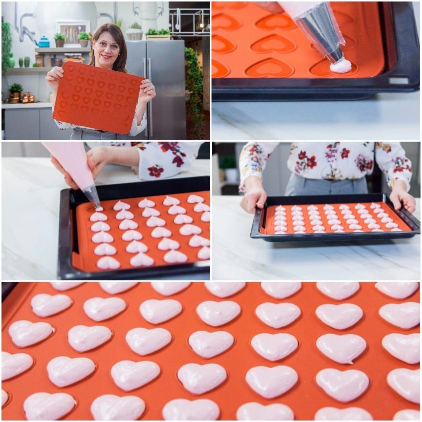 Macarons a cuore dressati con sac à poche su tappetino in silicone, pronti per il riposo