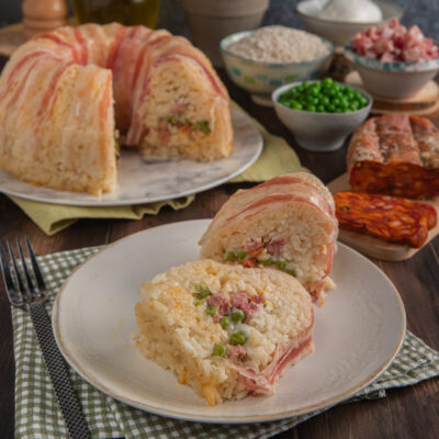 Timballo di riso avvolto in pancetta affettata, con ripieno di piselli e carne, servito a fette