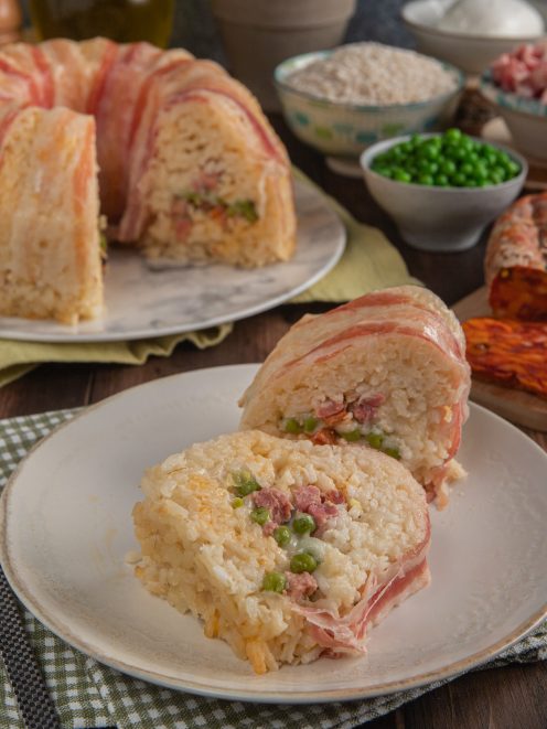 Timballo di riso avvolto in pancetta affettata, con ripieno di piselli e carne, servito a fette