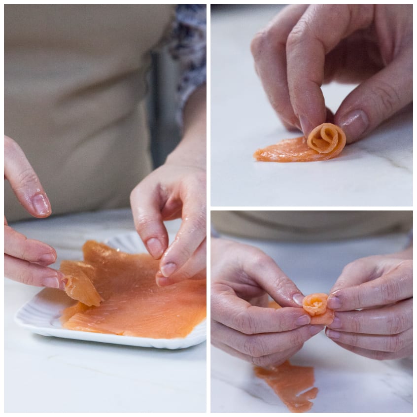 Mani che arrotolano fettine di salmone affumicato per formare piccole roselline