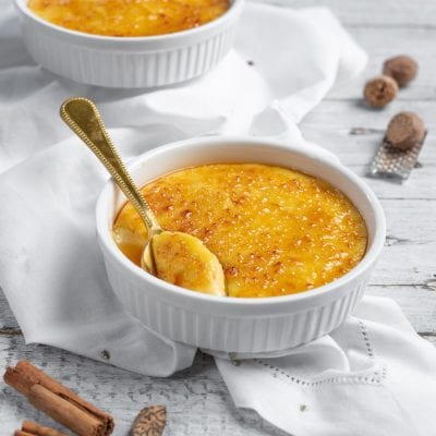 Crema catalana con superficie caramellata croccante e cucchiaio dorato che affonda nella crema