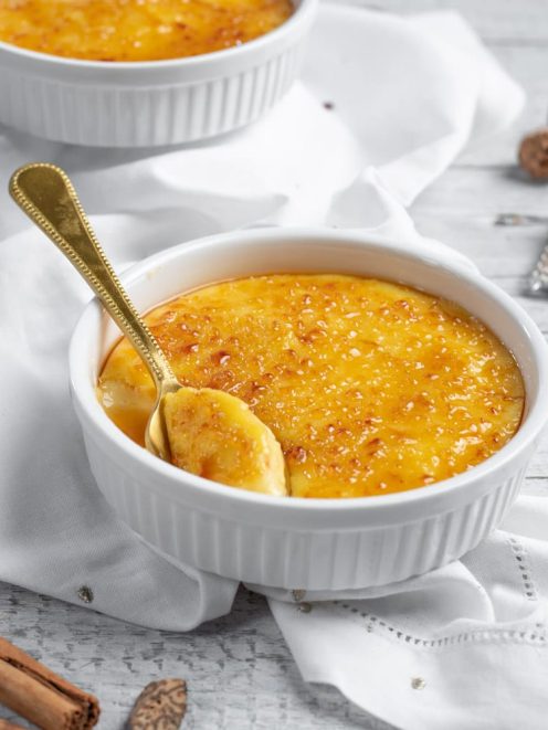 Crema catalana con superficie caramellata croccante e cucchiaio dorato che affonda nella crema