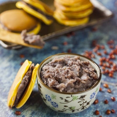 Confettura anko di fagioli azuki in una ciotolina, con chicchi sparsi e dorayaki sullo sfondo