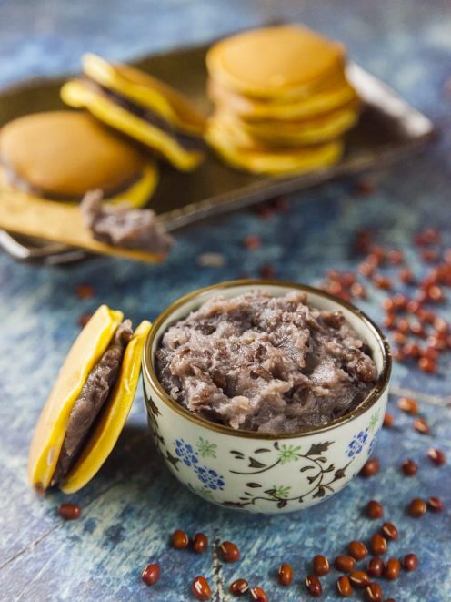 Confettura anko di fagioli azuki in una ciotolina, con chicchi sparsi e dorayaki sullo sfondo