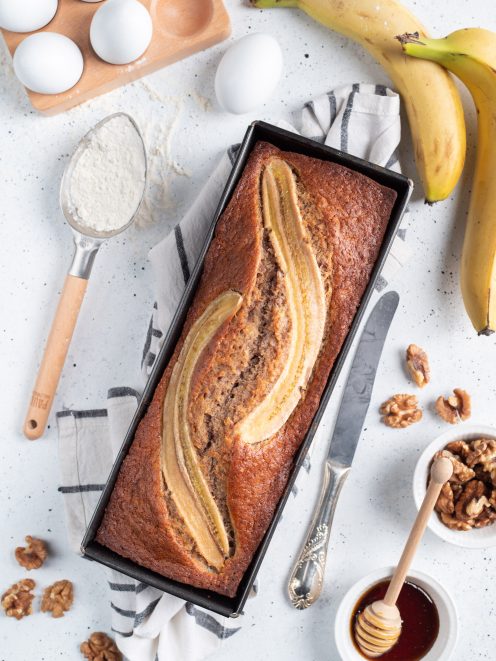 Banana bread appena sfornato con banana caramellata in superficie e noci intorno