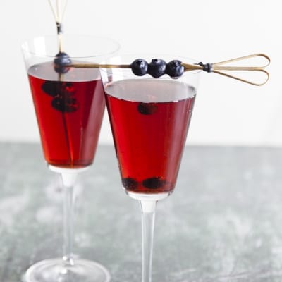 Kir cocktail servito in due calici con mirtilli freschi infilzati su stecchino decorativo