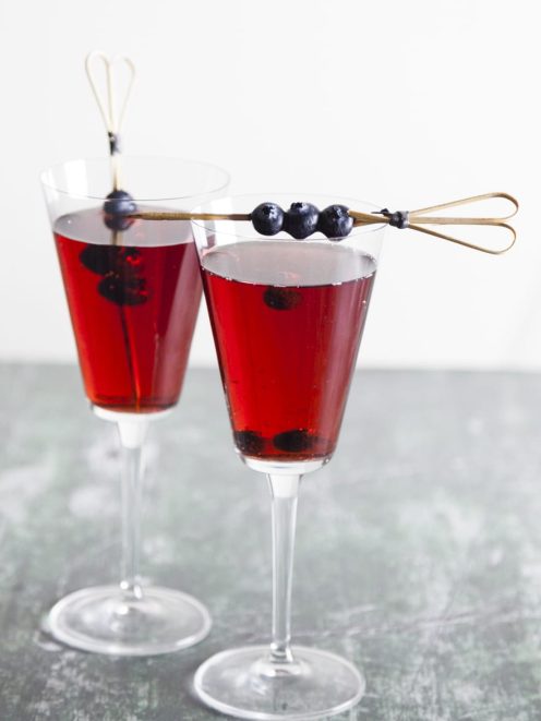 Kir cocktail servito in due calici con mirtilli freschi infilzati su stecchino decorativo