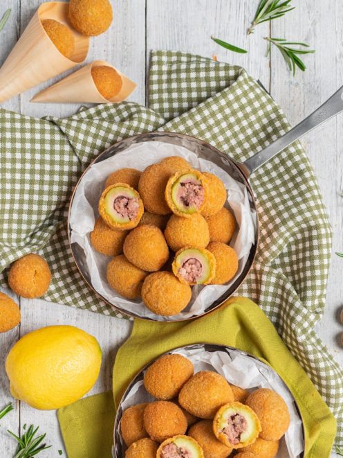 Olive all'ascolana fritte dorate servite in padella, alcune tagliate a metà per mostrare il ripieno di carne