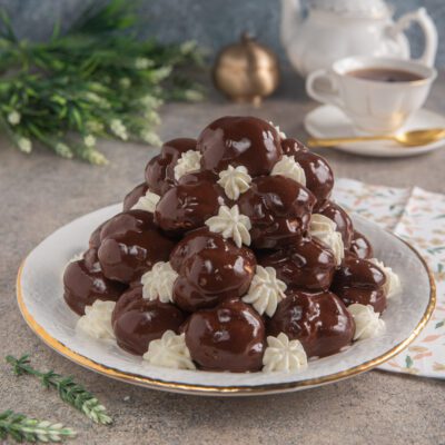 Profiteroles a piramide glassati al cioccolato fondente con ciuffetti di panna montata
