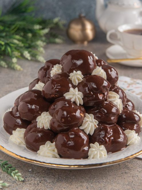Profiteroles a piramide glassati al cioccolato fondente con ciuffetti di panna montata