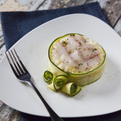 Risotto con branzino servito in un cestino di zucchine a nastro, con riccioli di zucchina e olio