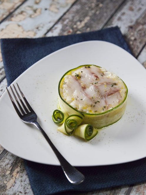 Risotto con branzino servito in un cestino di zucchine a nastro, con riccioli di zucchina e olio