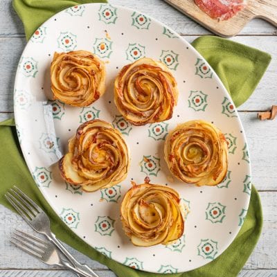 Roselline di patate al forno con speck, disposte a spirale su un vassoio da portata