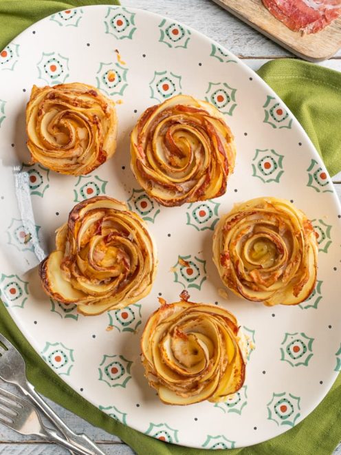 Roselline di patate al forno con speck, disposte a spirale su un vassoio da portata