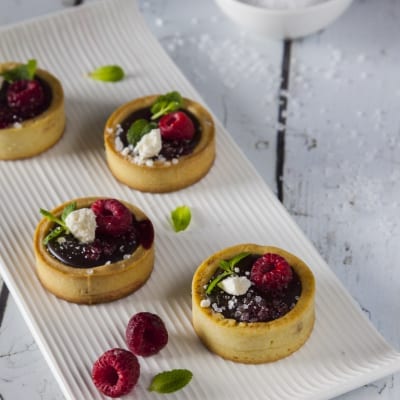 Tartellette con ganache al cioccolato e sale, guarnite con lamponi freschi e foglioline di menta