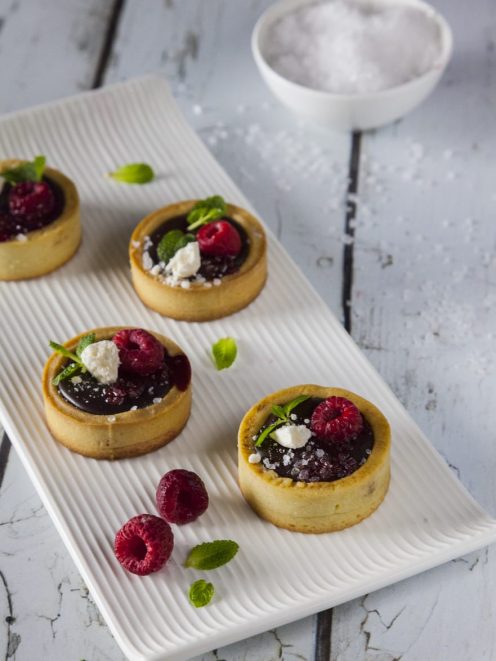 Tartellette con ganache al cioccolato e sale, guarnite con lamponi freschi e foglioline di menta
