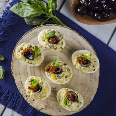 Uova ripiene alla greca guarnite con oliva nera, pomodoro secco e basilico fresco