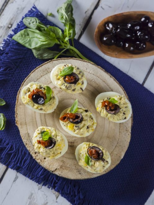 Uova ripiene alla greca guarnite con oliva nera, pomodoro secco e basilico fresco