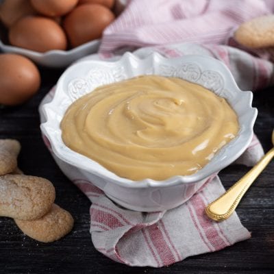 Crema pasticciera allo zabaione liscia e lucida, servita al cucchiaio con savoiardi accanto