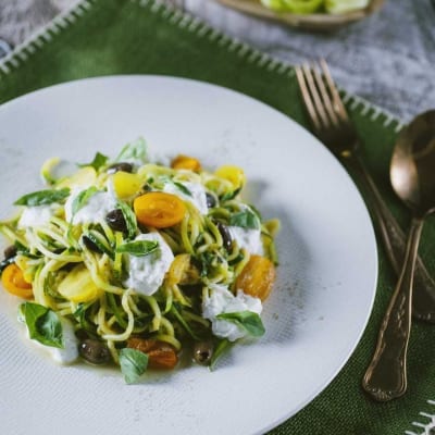 Spaghetti di zucchine con pomodorini gialli, olive, stracciatella e foglie di basilico fresco