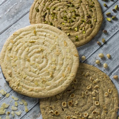 Tre dacquoise con motivo a spirale, guarnite rispettivamente con pistacchi, mandorle a lamelle e nocciole