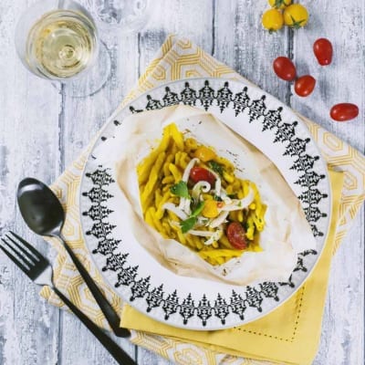 Strozzapreti al cartoccio con seppie, ceci e zafferano aperti nel piatto, con pomodorini e prezzemolo