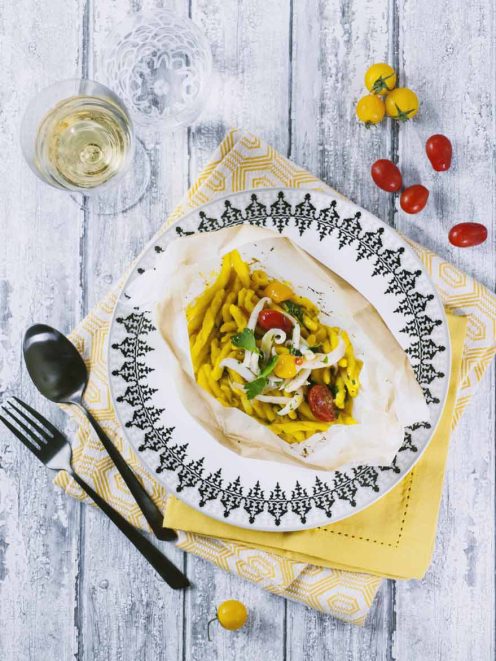 Strozzapreti al cartoccio con seppie, ceci e zafferano aperti nel piatto, con pomodorini e prezzemolo