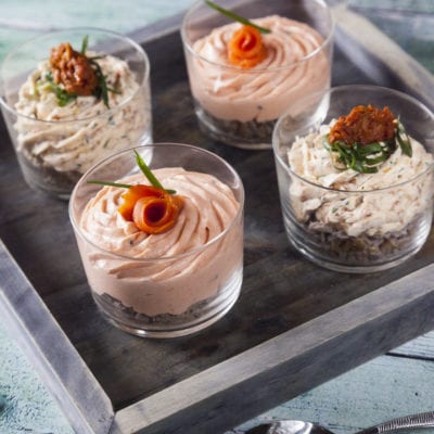 Mousse al salmone e mousse ai pomodori secchi servite in bicchieri, guarnite con salmone arrotolato ed erba cipollina