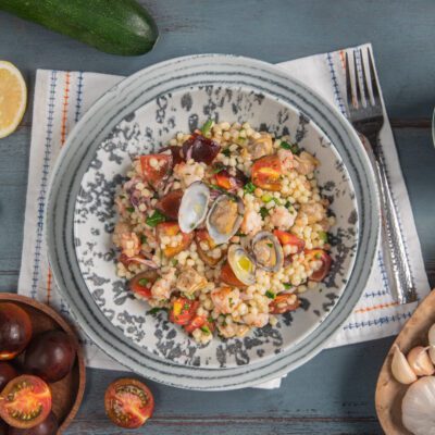 Fregola in insalata al sapore di mare con vongole aperte, gamberi, pomodorini e prezzemolo