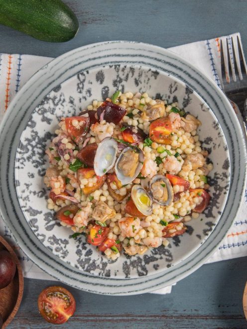 Fregola in insalata al sapore di mare con vongole aperte, gamberi, pomodorini e prezzemolo