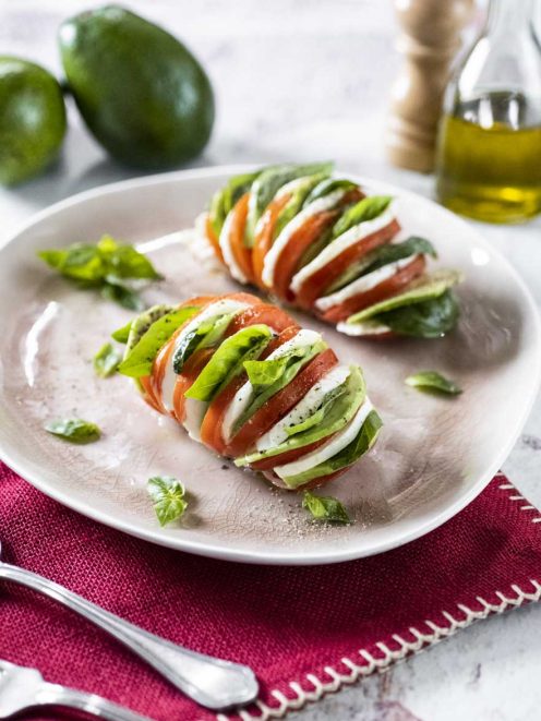 Pomodori hasselback con mozzarella, avocado e foglie di basilico fresco