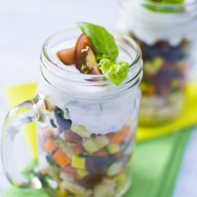 Macedonia salata in barattolo con verdure a cubetti, crema bianca e foglie di basilico fresco
