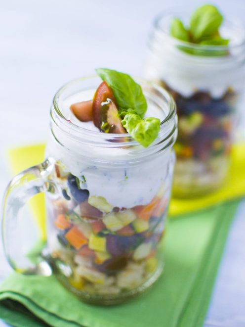 Macedonia salata in barattolo con verdure a cubetti, crema bianca e foglie di basilico fresco
