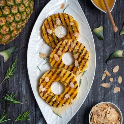 Ananas grigliato a fette con crema al centro, mandorle a lamelle e aghi di rosmarino