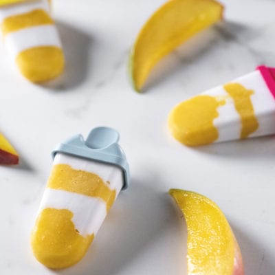 Ghiaccioli cocco e mango a strati bianchi e gialli, circondati da spicchi di mango fresco